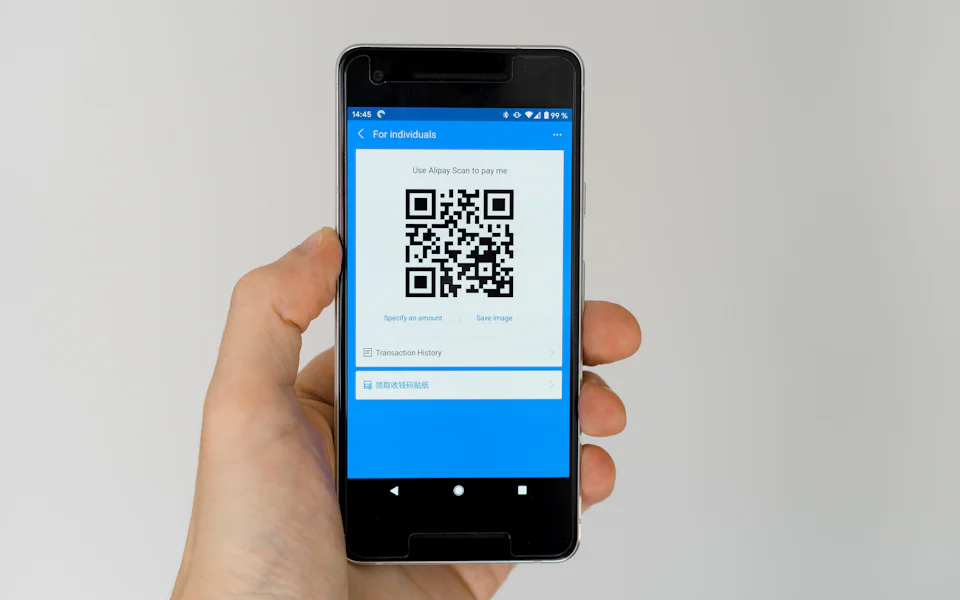 Hand holding a smartphone with a payment QR code on screen